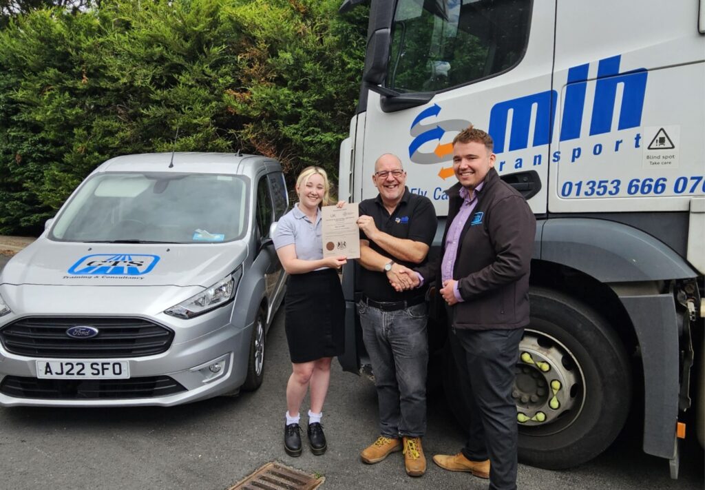 Matilda and Tom from CTS hand Nigel from MLH his Transport Manager CPC certificate, surrounded by vehicles from CTS and MLH.