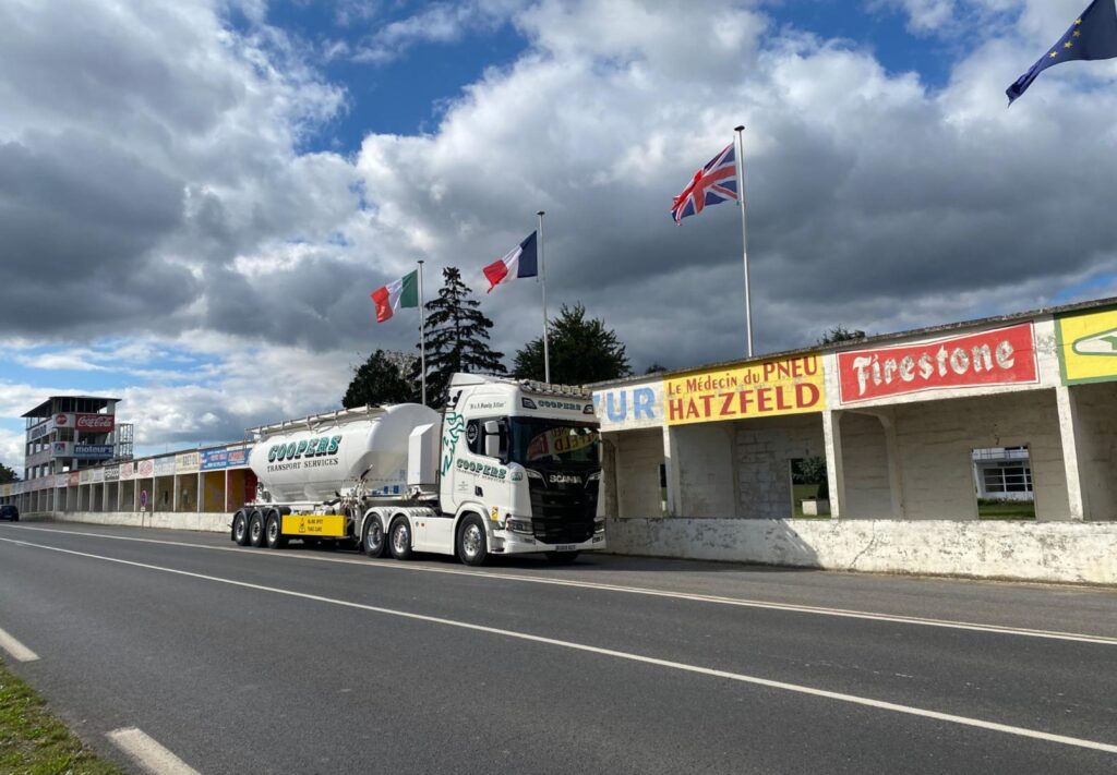 A Coopers lorry in front of the Italian flag, French flag and Union Jack.